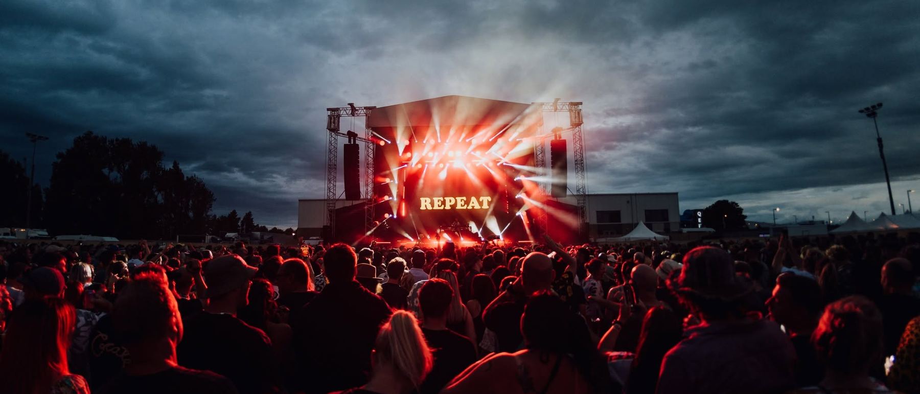 Festival crowd facing a lit stage under a stormy evening sky
